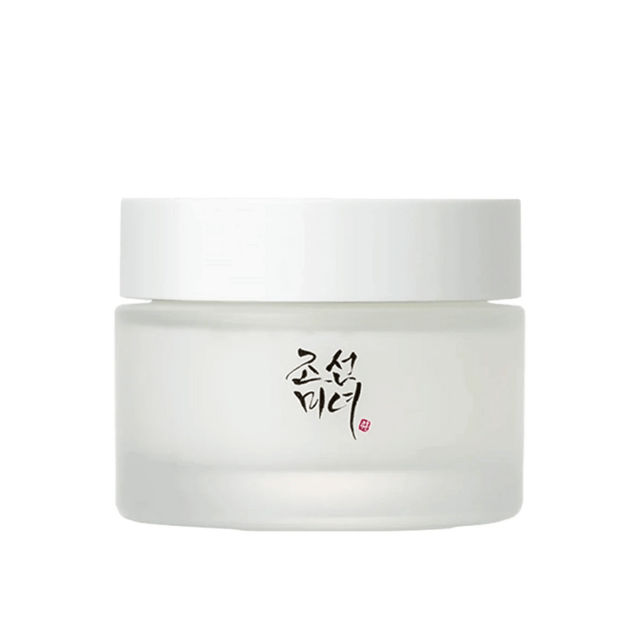 Bilden visar en burk "Beauty of Joseon Dynasty Cream". Förpackningen är i frostat glas med ett enkelt vitt lock, elegant dekorerat med traditionell koreansk kalligrafi i svart. Produkten är avsedd att erbjuda näringsrik hudvård inspirerad av gamla koreanska skönhetsrutiner.